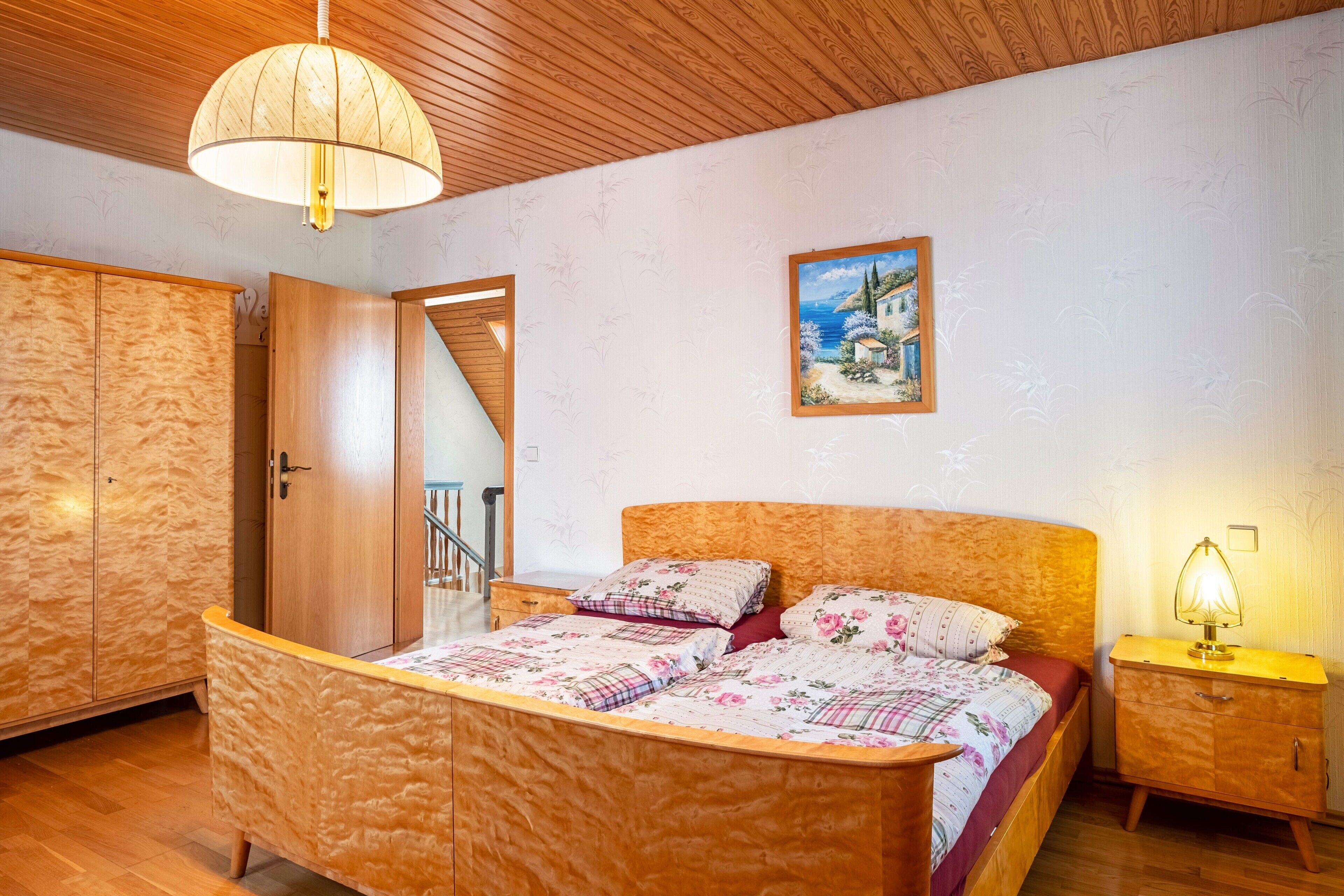 Une chambre à coucher avec un lit en bois, une table de chevet, une lampe, un tableau et une armoire en bois.