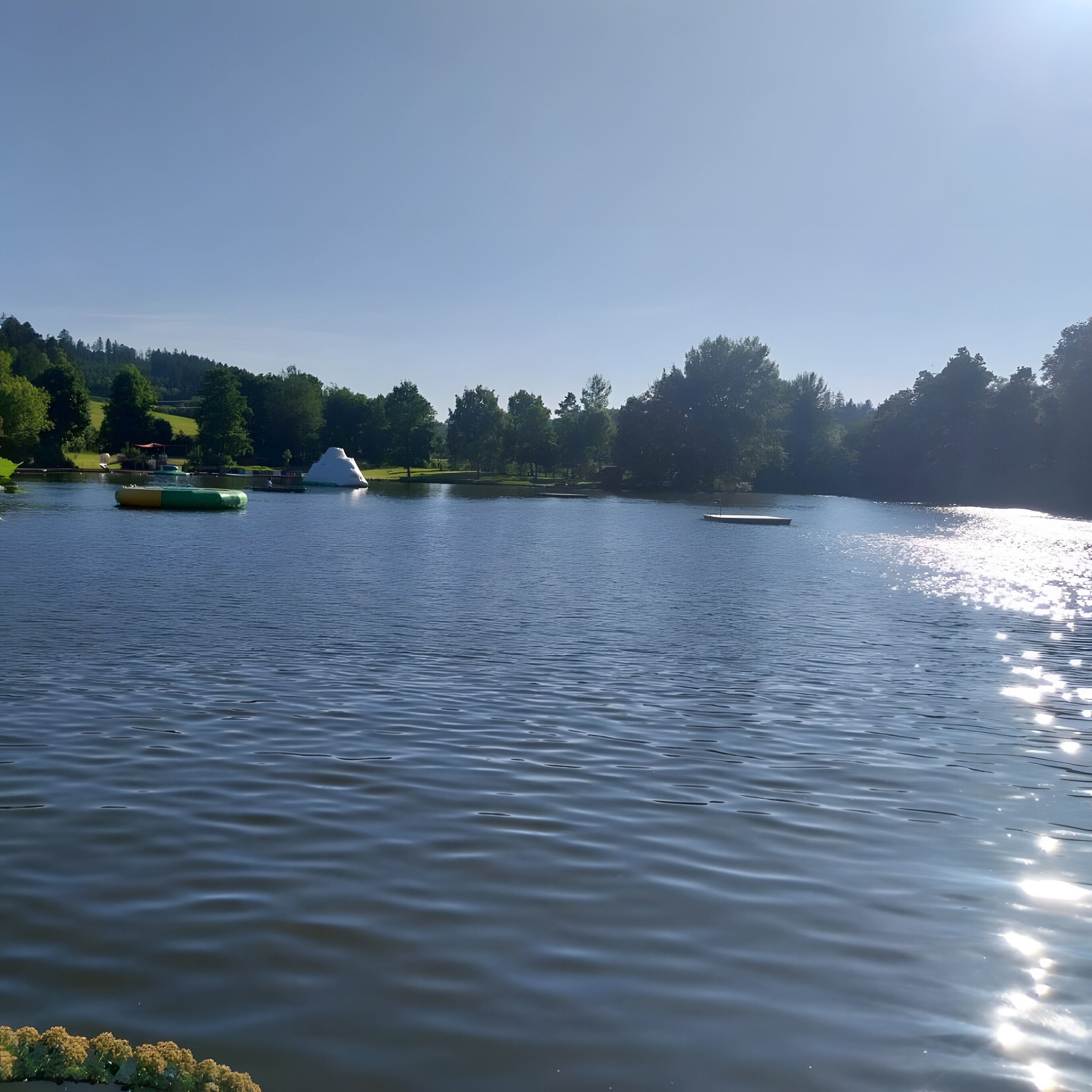 A calm lake with boats, a dock, and a forested hill in the background.