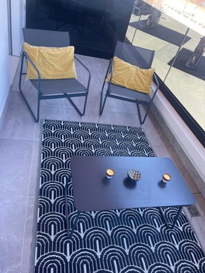 Un balcón con dos sillas, una mesa, un tapete estampado y vistas a través de un ventanal.