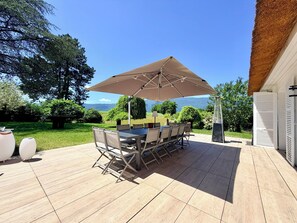 Un patio con mesa y sillas bajo un paraguas grande, rodeado de vegetación y vistas a las montañas.