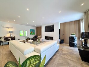 Un salon moderne avec un canapé blanc, une table basse en verre, un téléviseur à écran plat fixé au mur et un mur d’accent en bois.
