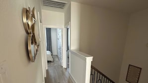 Ein Flur mit Holzboden, weißer Geländer und schwarzem Geländer, der zu einem Schlafzimmer mit Bett und Fenster führt.