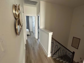Ein Flur mit Holzboden, weißer Geländer und schwarzem Geländer, der zu einem Schlafzimmer mit Bett und Fenster führt.