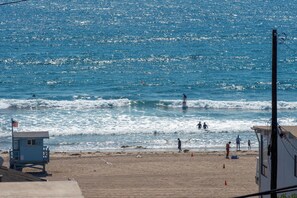 Ein Strand mit Wellen, einem Rettungsturm und einigen Personen.