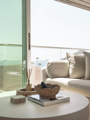 Ein modernes Wohnzimmer mit einem weißen Sofa, einem runden Couchtisch, einem Korbwäschesessel und einem Buch mit dem Titel 'Coastal California' auf dem Tisch.
