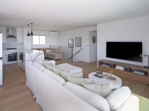 Ein modernes Wohnzimmer mit einer Couch, einem Fernseher und einem Essbereich mit Tisch und Stühlen.