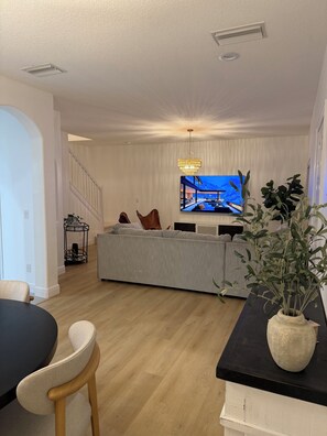 Ein modernes Wohnzimmer mit grauem Sofa, Fernseher, einer Kronleuchter und einer Treppe.