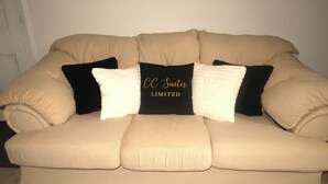 Un canapé beige agrémenté de trois coussins noirs et blancs, dont l’un porte l’inscription « CC Suites Limited ».