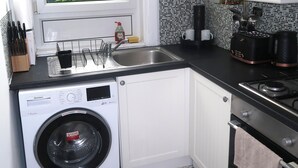 Une cuisine de taille réduite équipée d’un lave-linge, d’un évier et d’une cuisinière.