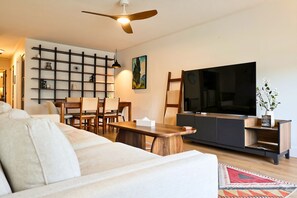 Un salon moderne avec un canapé, une table basse en bois, un téléviseur et une bibliothèque.