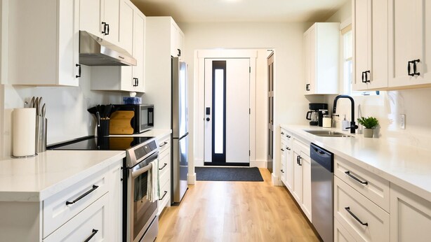 Una cocina moderna con armarios blancos, electrodomésticos de acero inoxidable y piso de madera.