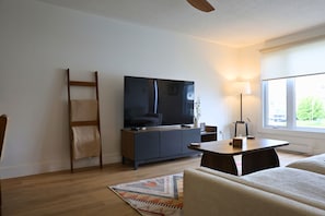 A living room with a TV, sofa, table, lamp, and windows.