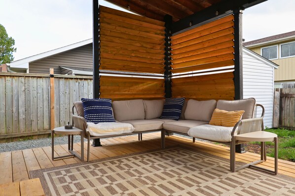 Une terrasse couverte avec un canapé d’angle, une petite table et un tapis à motifs.