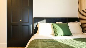 Una cama con cabecera oscura, una colcha estampada en verde y blanco, y una almohada verde.
