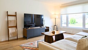 Una sala de estar moderna con una televisión de pantalla plana, un ventilador de techo, un sofá, una mesa de centro y un ventanal grande.
