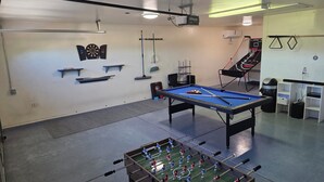 Ett rum med ett biljardbord, ett fotbollsspel, en darttavla, hyllor och en basketkorg.