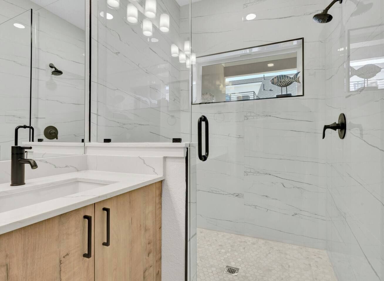A modern bathroom with a glass-enclosed shower, a white marble wall, and a wooden vanity.