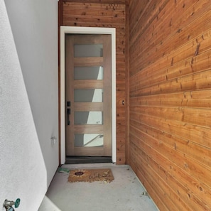 A wooden door with frosted glass panels, a doormat with a sun design, and a white wall adjacent to the door. - Bright Dallas 3BR | Rooftop, Garage, Backyard - Holiday Home (Dallas)