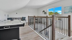 Uma sala de estar moderna com mesa de bilhar, um sofá e escada que leva a uma varanda com vista.