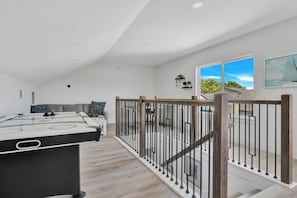 A modern living room with a pool table, a sofa, and a staircase leading to a balcony with a view. - Bright Dallas 3BR | Rooftop, Garage, Backyard - Holiday Home (Dallas)