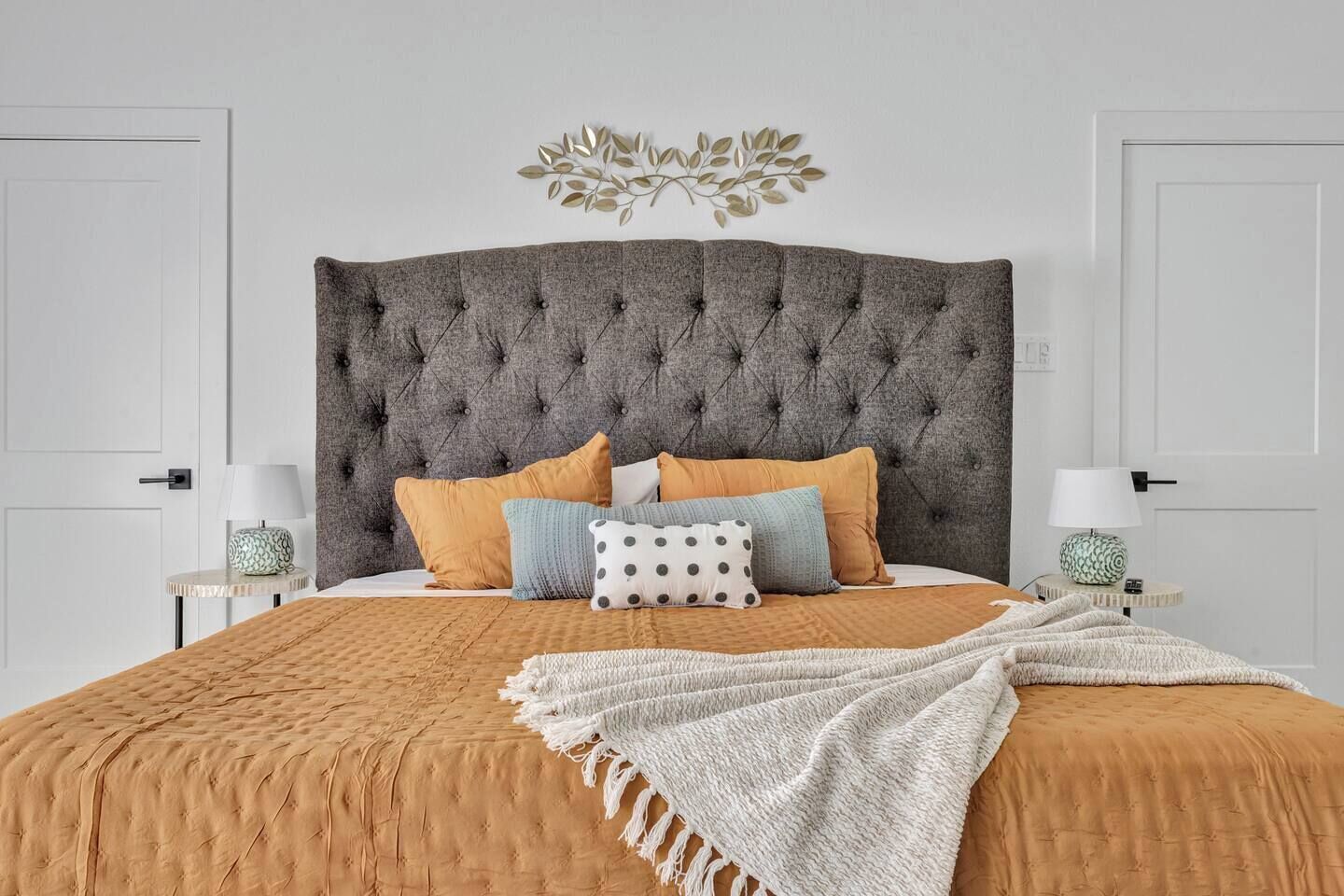 A bedroom with a tufted headboard, a bed with multiple pillows, a throw blanket, and two bedside tables with lamps.