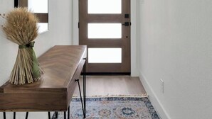 Um corredor com porta de madeira, espelho e mesa com um vaso de plantas secas.