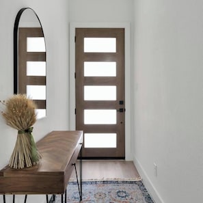 A hallway with a wooden door, a mirror, and a table with a vase of dried plants. - Bright Dallas 3BR | Rooftop, Garage, Backyard - Holiday Home (Dallas)