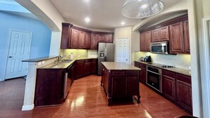 A modern kitchen with wooden cabinets, stainless steel appliances, and a large island. - Near FIFA World Cup Dallas Stadium, Golf view home (Grand Prairie)