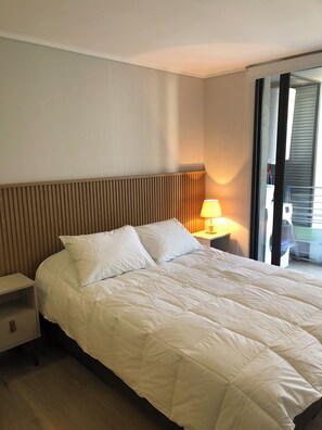 A hotel room with a bed, a nightstand, a lamp, and a view of the outside. - Cozy 1-bedroom apartment with AC in brilliant Las Condes (Las Condes)