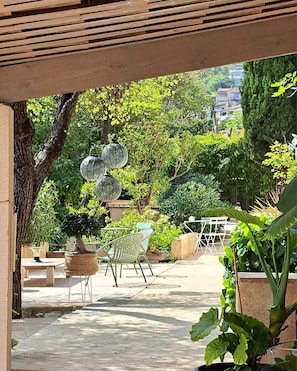 Un espacio al aire libre con patio, una pérgola, plantas en macetas, una zona de estar con sillas y un farol esférico decorativo.