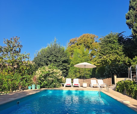 A swimming pool with lounge chairs and an umbrella, surrounded by greenery and trees.. Bastide de Marie Grasse - Charming Bed and Breakfast - Pool