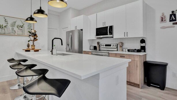 Een moderne keuken met witte kasten, roestvrijstalen apparatuur, een centraal eiland met barkrukken, hanglampen en een koffiehoek.
