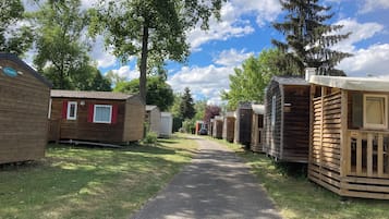 Une rangée de maisons mobiles en bois, séparées par un chemin pavé, entourées d’arbres et sous un ciel dégagé.