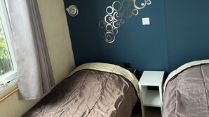 Un dormitorio con dos camas, una ventana con cortinas, un estante en la pared y un adorno metálico.