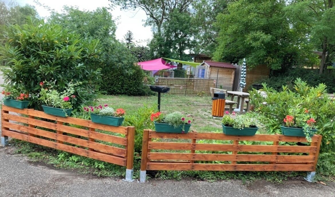 Une clôture en bois agrémentée de jardinières, un petit abri de jardin et un banc, le tout dans un cadre verdoyant.