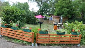 Una cerca de madera con jardineras, un cobertizo pequeño y un banco en un jardín.