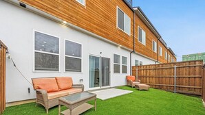 Een achtertuin met een wit huis, een houten terras, een groen gazon en tuinmeubilair.