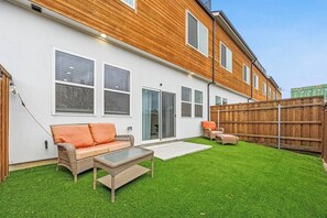 Ein Wohngrundstück mit einem weißen Haus, einer Holzterrasse, einem grünen Rasen und Gartenmöbeln.