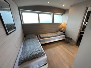 Ein kleines Zimmer mit zwei Betten, einem kleinen Tisch, einer Lampe und einem Fenster.