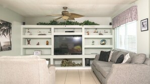 Ein Wohnzimmer mit Flachbildfernseher, Deckenventilator und Regalen mit Dekoration.