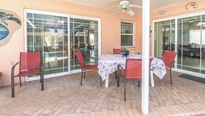 Eine Terrasse mit Tisch und Stühlen, einem Deckenventilator und großen Glasfenstern, die zu einem Außenbereich führen.