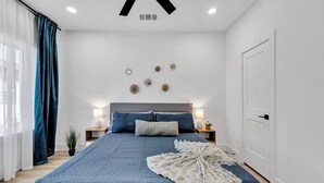 A bedroom with a large bed, bedside tables, a ceiling fan, and a door. - Fresh Modern 3BR • Rooftop • 5 min to Downtown (Dallas)