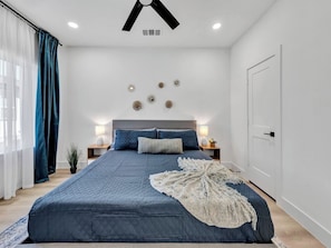 Ein Schlafzimmer mit einem großen Bett, Nachttischen, einem Deckenventilator und einer Tür.