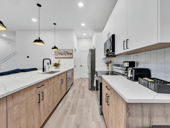 Eine moderne Küche mit Holzschränken, einer weißen Arbeitsplatte und einer Kaffeebar.