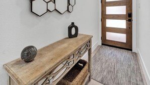 A hallway with a wooden console table, a hexagonal mirror wall, and a wooden door. - Fresh Modern 3BR • Rooftop • 5 min to Downtown (Dallas)