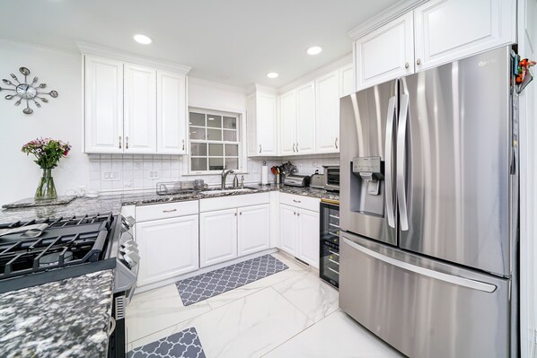A modern kitchen with white cabinets, stainless steel appliances, and a marble countertop.