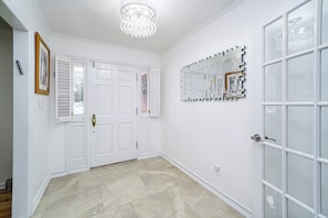 A hallway with white doors, a chandelier, and a decorative mirror.