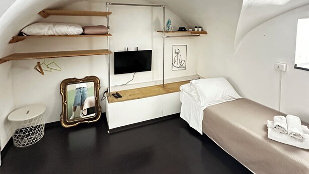 A compact, arched room with a bed, a small desk, a TV, and a mirror. - Spàzio apartments Duomo I (Catania)