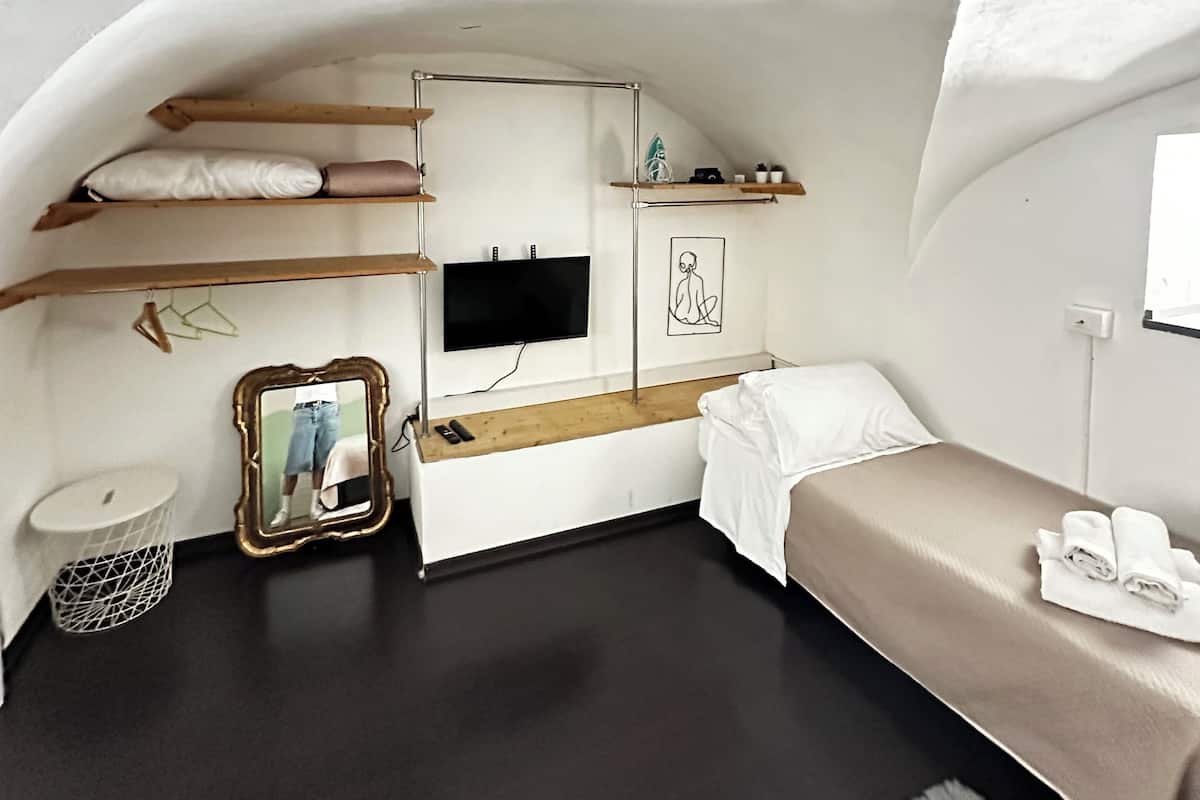 Une pièce compacte à voûte, comprenant un lit, un petit bureau, un téléviseur et un miroir.