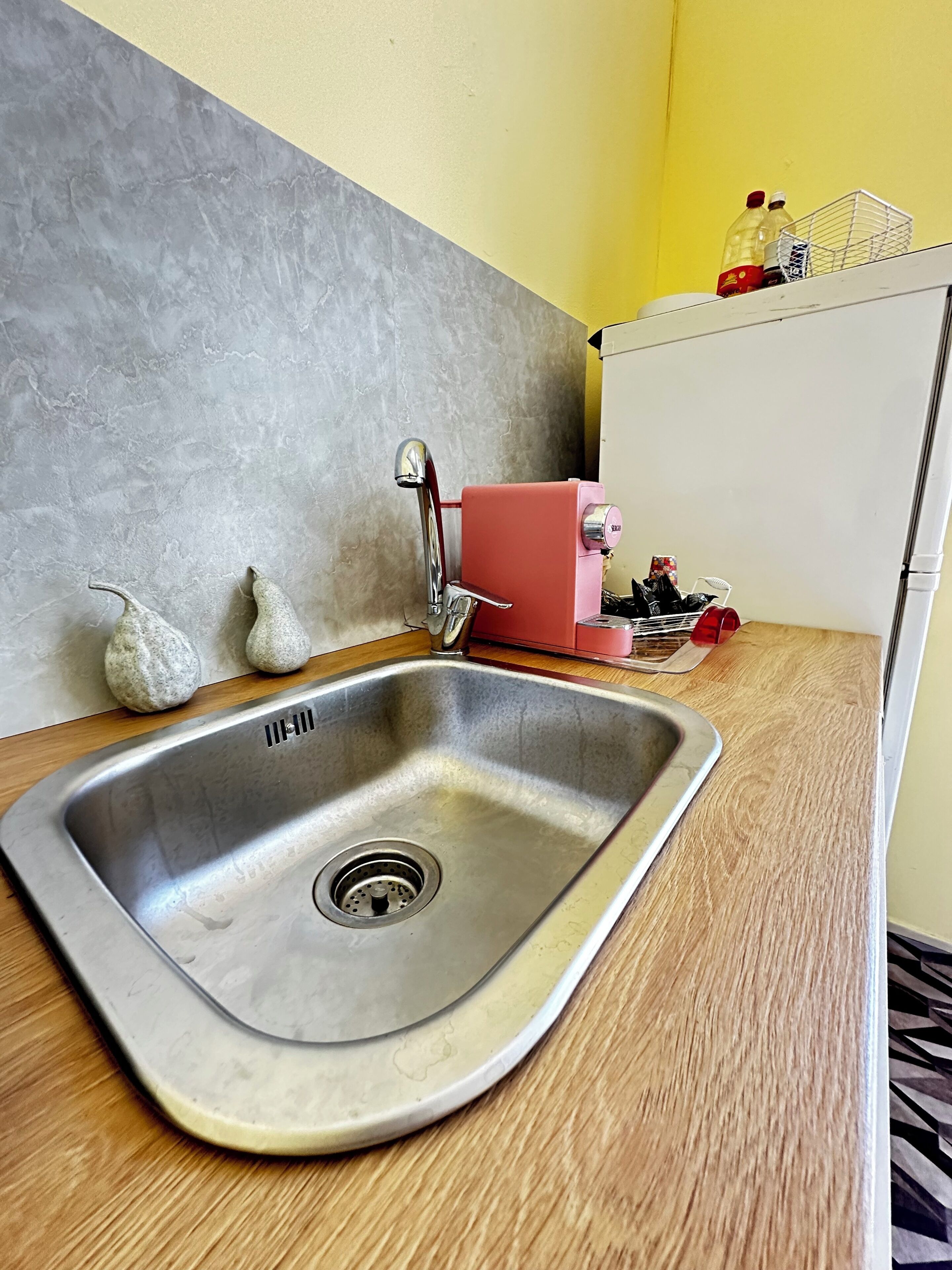 A kitchen with a stainless steel sink, a red appliance, and a white cabinet with bottles and a basket.